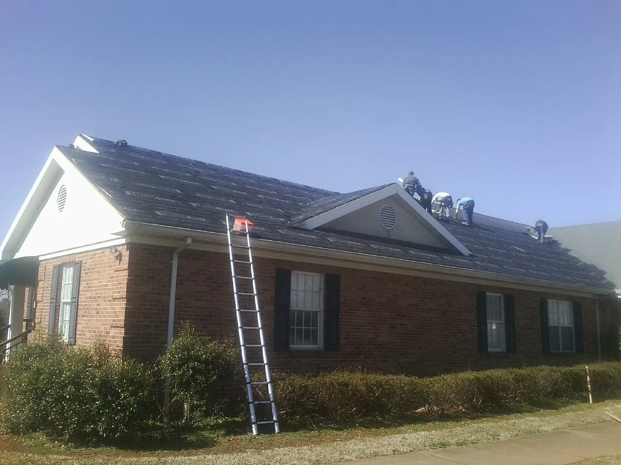 Crew tearing shingles off a brick ranch roof with a ladder set — Emergency Roof Repair work by our crew in Belle Plaine