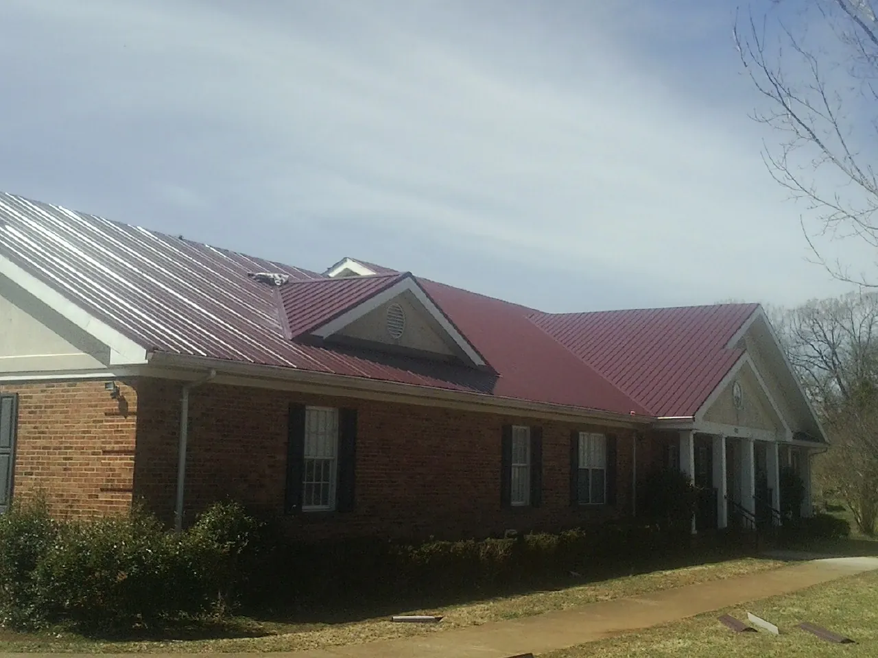 Red metal roof with gabled entries on a long brick building, from a Hail Damage Roof Repair job in Belle Plaine