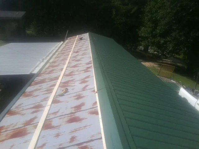 Old rusted panels beside newly installed green metal roofing — Wind Damage Roof Repair by Roofing Brothers in Belle Plaine