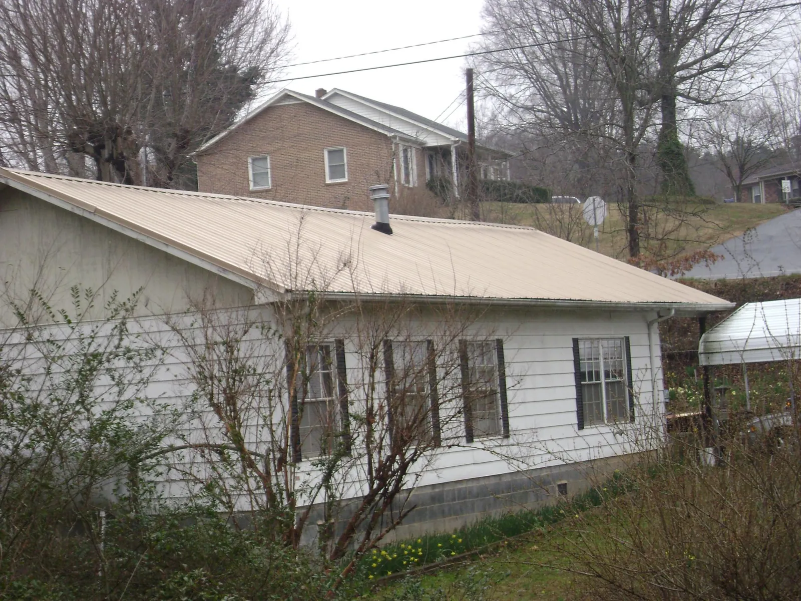Tan metal roof on a white sided house set into a hillside — Commercial Roofing by Roofing Brothers in Belle Plaine
